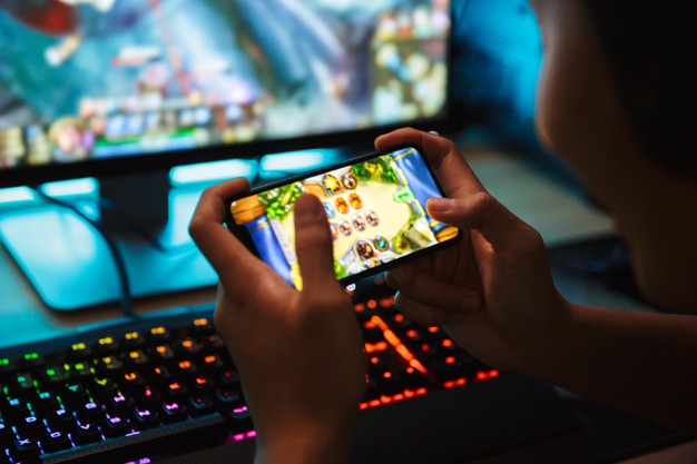 portrait-teenage-gamer-boy-playing-video-games-smartphone-computer-dark-room-wearing-headphones-using-backlit-colorful-keyboard